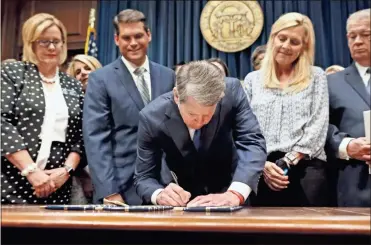  ??  ?? Georgia’s Republican Gov. Brian Kemp, center, signs legislatio­n in Atlanta, banning abortions once a fetal heartbeat can be detected, which can be as early as six weeks before many women know they’re pregnant. Georgia became the fourth state to enact the ban on abortions after a fetal heartbeat can be detected.