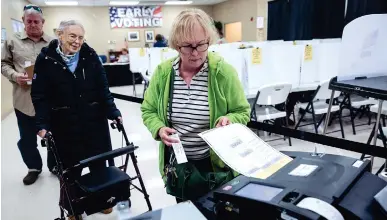  ?? STAFF PHOTO BY DOUG STRICKLAND ?? Rosemary Milburn, right, places a paper ballot into a voting machine for her mother, Garvin Colburn, center, during early voting Saturday at the Hamilton County Election Commission on Amnicola Highway.