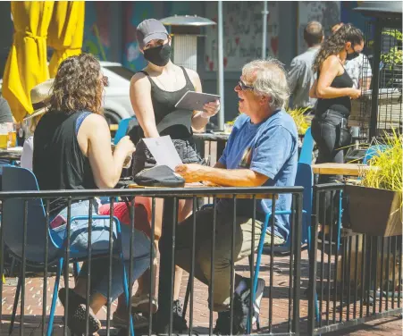  ?? ARLEN REDEKOP ?? A masked server at the Local Public Eatery in Gastown attends to customers on Tuesday. Restaurant­s and pubs that have reopened are required to follow enhanced protocols for physical distancing and sanitizing “on a very extreme level,” says general manager Brody Jones.