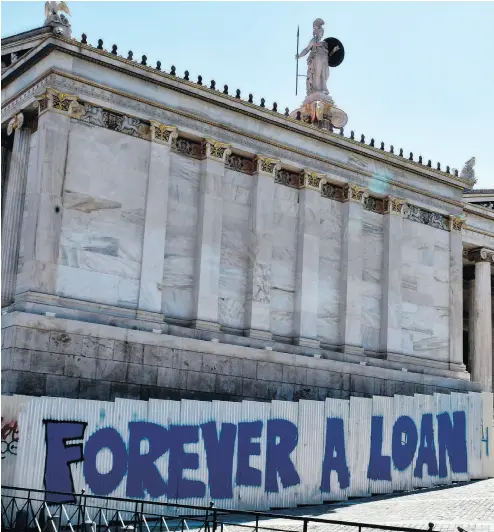  ?? LOUISA GOULIAMAKI / AFP / GETTY IMAGES FILES ?? A woman walks past a graffiti referring to the Greek debt during the height of the country’s debt crisis last August.