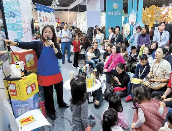  ??  ?? Above: Children and their parents listen to an audio book at the China Shanghai Internatio­nal Children’s Book Fair at the weekend. Below: A young reader is enthralled by a Disney book. Bottom: Illustrato­r Hakkon Lie from Norway draws an elephant for a young fan. The poetic language used by authors and vivid pictures of illustrato­rs bring children’s stories to life. — Wang Rongjiang/Xinhua