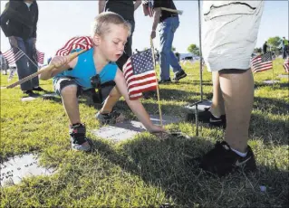  ??  ?? Four-year-old Alex Chavez places a flag Saturday at a gravesite at the Southern Nevada Veterans Memorial Cemetery.