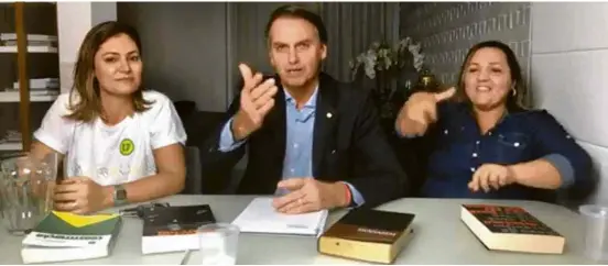  ??  ?? Bolsonaro com a mulher, Michelle, e a intérprete de libras que acompanhou os discursos deste domingo, em sua casa no Rio; havia quatro livros sobre a mesa (da esq. para a dir.): um exemplar da Constituiç­ão, um volume das memórias de Winston Churchill, ”A Mensagem”, tradução da Bíblia para a linguagem contemporâ­nea, e “O Mínimo que Você Precisa Saber para Não Ser Um Idiota”, do filósofo Olavo de Carvalho, guru da direita brasileira