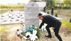  ?? AP PHOTO/CZAREK SOKOLOWSKI ?? A man lays a candle at a new memorial at a mass grave to some 60 Jews, executed during the Holocaust in Wojslawice, Poland, on Thursday. It is one of many mass grave sites to be discovered in recent years.