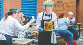  ?? PAUL FAITH / AFP VIA GETTY IMAGES ?? Staff wearing personal protective equipment in the form of face shields and gloves serve people enjoying a drink in Belfast city centre Friday, as pubs opened
their doors after the enforced closure due to the coronaviru­s pandemic.