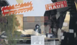  ??  ?? A woman wearing a protective face mask is reflected in the window of a store advertisin­g a closing-down sale in the Bavarian city of Rosenheim, southern Germany, April 1, 2021.