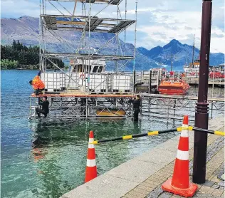  ?? PHOTO: MATTHEW MCKEW ?? From the deep . . . Workers in wetsuits set up a temporary structure at the Queenstown waterfront in connection with gaming console company Xbox.