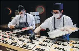  ??  ?? Workers sort boxes of prepared meals at Basketball City in New York. Kissaki chefs Evan Zagha, left, and Kazusa Shimiz prepare sushi meals for Mount Sinai Medical Center.