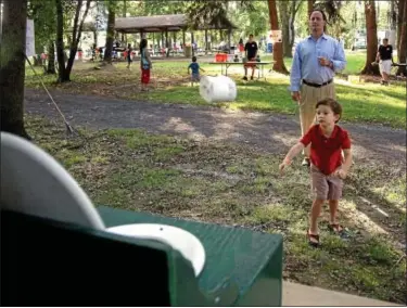  ?? Gazette staff photos by BOB RAINES ?? Andrew Byrne tosses a roll of toilet tissue at a toilet bowl target at the Whitpain Camp Carnival while his dad, Steve, looks on.