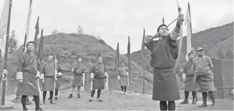  ??  ?? (Top) Bhutanese archers watch another take aim at the target. (Left) An arrow maker heats a bamboo stick as he makes an arrow at the Bhutan Traditiona­l Archery shop. (Bottom) An archer points to a target hit by an arrow.