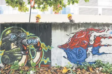  ??  ?? Constructi­on workers (top) walk behind a mural dedicated to missing Malaysia Airlines flight MH370, on a wall next to a parking lot in Kuala Lumpur. — AFP photo