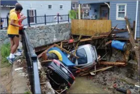  ?? DAVID MCFADDEN — THE ASSOCIATED PRESS ?? Residents gather by a bridge to look at cars left crumpled in one of the tributarie­s of the Patapsco River that burst its banks as it channeled through historic Main Street in Ellicott City, Md., Monday. Sunday’s destructiv­e flooding left the former...