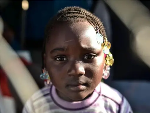  ?? (AFP/Getty) ?? A Malian refugee child poses from behind a fence in a makeshift camp