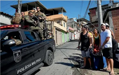  ?? AP ?? Police ride past as residents carry a body to a waiting vehicle after a police operation that resulted in multiple deaths in the Complexo do Alemao favela in Rio de Janeiro, Brazil.