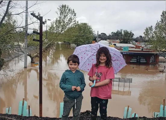  ?? Photo: Max Stainkamph ?? High ground: Madi O’Shea, 8, and Logan O’Shea, 6, on the rail line above a flooded Tallarook St on Friday morning in Seymour.