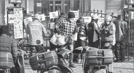  ?? FENG YONGBIN / CHINA DAILY ?? Delivery workers wait to pick up meals at a food street in Beijing on Tuesday. The demand for food delivery has soared with many people quarantine­d at home for COVID-19 control.