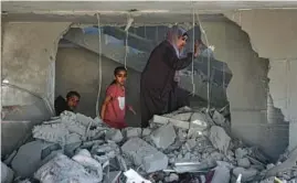  ?? GETTY-AFP ?? A Palestinia­n woman and children step through rubble Saturday in a house hit by an Israeli airstrike in Rafah, in the Gaza Strip. At least nine people died, authoritie­s said.