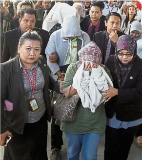  ??  ?? Camera shy: Fauziah, Ag Mohd Tahir and Lim covering their faces as they are escorted into court in Kota Kinabalu.