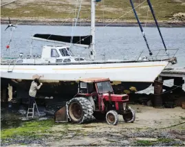  ??  ?? Sailboat maintenanc­e, Falklands style: Leiv Poncet works on Peregrine (top) at the Beaver Island jetty. Elias and Eric take in the sunshine at the perhaps grandiosel­y named airstrip.