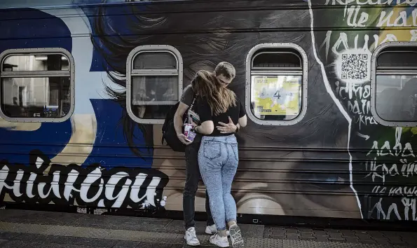  ?? PHOTO: GETTY IMAGES ?? Fare well . . . A couple hugs by one of the cars of the ‘‘Train to Victory’’ in Kyiv, Ukraine. The ‘‘Train to Victory’’ project, which will travel to different parts of the country, features seven train cars painted by Ukrainian artists, each car telling stories of people resisting Russian forces.