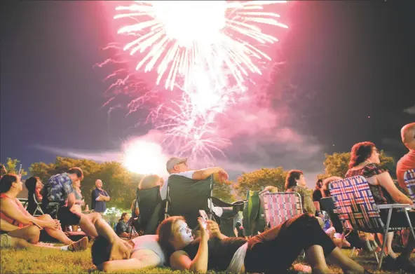  ?? Christian Abraham / Hearst Connecticu­t Media ?? Above, Donna Catalano and Ari Karagianni­s, of Shelton, watch the Derby/ Shelton Fourth of July fireworks from Veterans Park in Shelton on July 3, 2019. At right, part of the fireworks exhibition at Calf Pasture Beach in Norwalk that same night.