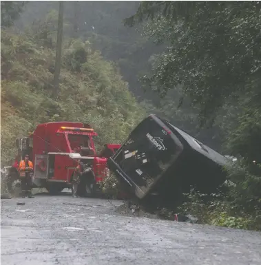  ?? CHAD HIPOLITO / THE CANADIAN PRESS ?? Search and rescue crews and RCMP help a tow-truck crew remove a bus from the ditch of a logging road near Bamfield, B.C., on Saturday where two University of Victoria students died and several others were injured.