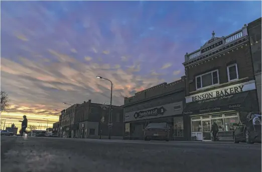  ?? DAVID GOLDMAN/AP PHOTOS ?? A customer carries a box of baked goods from a bakery at sunrise in Benson, Minn., a small prairie town where two neighbors — in their own, well-kept, century-old homes — can live in vastly different worlds.