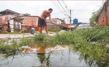  ??  ?? André da Silva improvisa com a enxada para a água dachuvaeo esgoto não entrarem em casa; ruas do Morro do Pau Branco estão precárias