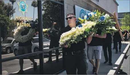  ?? Gina Ferazzi Los Angeles Times ?? RIVERSIDE COUNTY sheriff’s deputies and CHP officers carry flowers in honor of Officer Andre Moye to the Riverside CHP station.