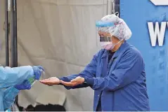  ?? ASSOCIATED PRESS FILE PHOTO ?? Theresa Malijan, a registered nurse, has hand sanitizer applied earlier this month after she removed gloves following testing at a drive-thru COVID-19 testing station for University of Washington Medicine patients in Seattle. The critical shortage of testing swabs, protective masks, surgical gowns and hand sanitizer can be tied to a sudden drop in imports of medical supplies.