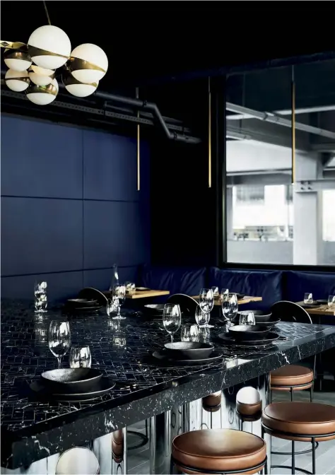  ??  ?? Above — A generous communal table topped with nero marquina herringbon­e tiles anchors the open-plan space, drawing visitors to congregate centrally.