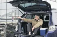  ??  ?? Yi Bai, of Dunedin, shelters from the rain in the back of his station wagon as he fishes for salmon and blue cod in Wharf St yesterday.