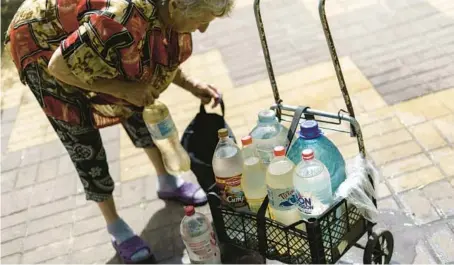  ?? DAVID GOLDMAN/AP ?? Lyubov Mahlii, 76, packs a crate with water bottles she filled at a public tank to take back to her apartment on Aug. 6 on Sloviansk, Ukraine.