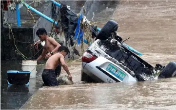  ?? — Reuters photo ?? Residents fetch water next to a submerged vehicle swept by flash floods along a river bank in Marikina, Metro Manila.