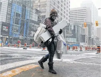  ?? REUTERS ?? A shopper carries Christmas purchases a day before coronaviru­s disease restrictio­ns are reintroduc­ed to regions of the Greater Toronto Area (GTA) as snow falls in midtown Toronto.