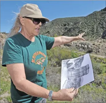  ?? Dan Watson/The Signal ?? Community Hiking Club Executive Director Dianne Erskine-Hellrigel points to the remaining piece of the St. Francis Dam as she holds a copy of an old photo of the same area and the “tombstone” — the center portion of the dam that was left standing after the break on March 12, 1928.