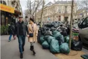  ?? AP PHOTO/LEWIS JOLY ?? People walk past a pile of garbage in Paris on March 13 as protests continue with uncollecte­d trash piling higher by the day.