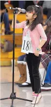  ??  ?? Ernest Stapleton Elementary School third-grader Sofia Alcocer stands on her toes to reach the microphone while participat­ing in Friday’s spelling bee.