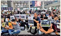  ??  ?? Protesters sit on the floor and hold pro-democracy posters and banners for tourists arriving in their city