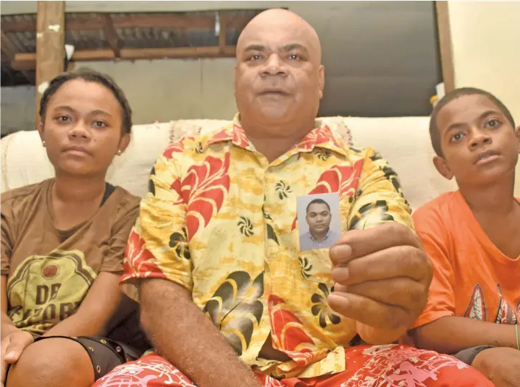  ?? Photo: Waisea Nasokia ?? Costello Tabulawaki holds a picture of his eldest son, Ilaisa Nabou, while daughter Nanise Lewatu and Jovesa Tomasi look on at their residence in Sabeto, Nadi, last night. Mr Nabou, a Radisson Blu Resort chef, was swept away while trying to cross a flooded river in Sabeto.