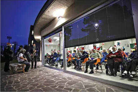  ?? (AP Photo/Luca Bruno) ?? Hosts, protected by a glass window, attend a Christmas concert at the Martino Zanchi nursing home Saturday in Alzano Lombardo, one of the areas in northern Italy that suffered the most in the first wave of COVID-19, as the hosts celebrate Christmas.