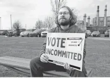  ?? Reuters-Yonhap ?? Listen To Michigan volunteer Eric Peter-Bull sits outside a polling station, holding a sign that encourages people to vote uncommitte­d as Democrats and Republican­s during Michigan primary presidenti­al election in Dearborn, Mich., Tuesday.