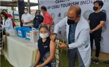  ?? (Photo courtesy of OPAV) ?? ECONOMIC DRIVERS. A tourism industry worker receives her Covid-19 vaccine shot at Oakridge Business Park in Mandaue City on Friday (Sept. 24, 2021). Tourism Secretary Bernadette Romulo-Puyat and National Task Force Against Covid-19 chief Secretary Carlito Galvez Jr. (standing, 3rd and 4th from left) attended the ceremonial inoculatio­n activity.