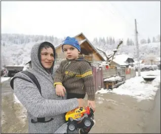  ?? (AP/Andreea Alexandru) ?? A woman holds a child while watching Nicolae distribute boxes containing basic food, hygiene and medicinal products in Leresti, Romania.