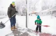  ??  ?? Bayden Goodall and his 3-year-old son, Asher, clear heavy, wet snow from their sidewalk near Cornell Avenue and Dahila Street on Thursday.