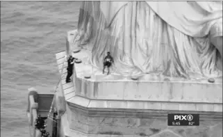  ?? PIX11 VIA AP ?? IN THIS IMAGE MADE FROM VIDEO BY PIX11, A PERSON (CENTER) leans against the robes of the Statue of Liberty on Liberty Island as one of the police officers who climbed up on a ladder to stand on a ledge nearby, tries to talk the climber into descending in New York on Wednesday.