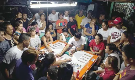  ?? — AFP ?? Relatives and visitors participat­ing in a card game to raise money for the funeral of an alleged drug dealer gunned down by unidentifi­ed men in Manila.