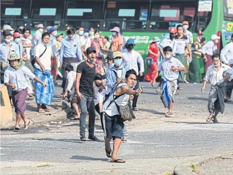  ?? AFP ?? A pro-military supporter, centre, uses a sling shot to fire projectile­s at residents during a rally in Yangon yesterday, following weeks of mass demonstrat­ions against the military coup.