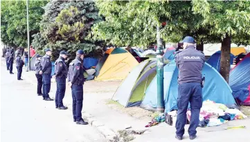  ??  ?? Bosnian police officers stand guard as migrants pack their belongings and their tents, during the evacuation of a makeshift camp in a park across the City Hall, in Sarajevo in order to relocate them in southern Bosnia. — AFP photo