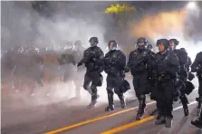  ?? NATHAN HOWARD/ASSOCIATED PRESS ?? Portland police officers walk through the Laurelhurs­t neighborho­od after dispersing protesters from Multnomah County Sheriff’s Office early in the morning on Saturday.